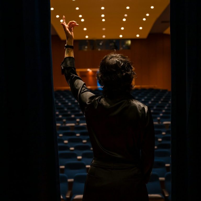 Rednerin für Impulsvorträge und Workshopleitung Person in formeller Kleidung hebt die Hand vor einem leeren Veranstaltungsraum.
