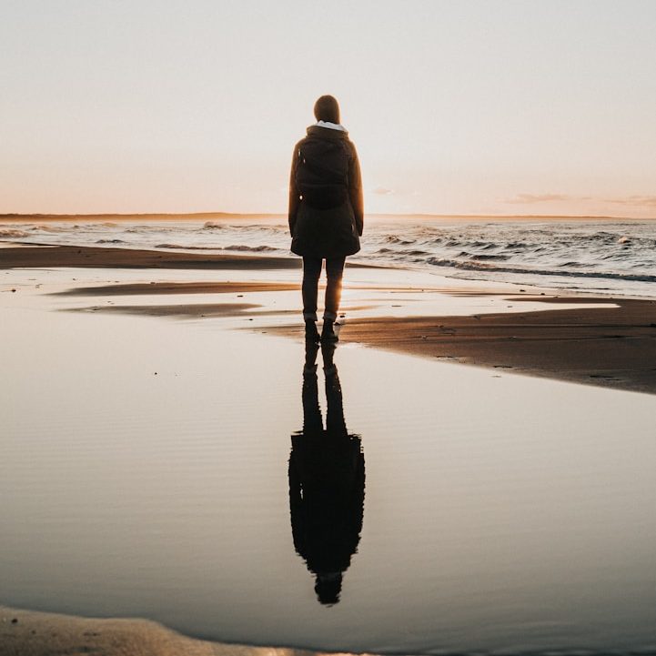 Personal Coaching in Göttingen und deutschlandweit Eine Person steht am Strand und schaut auf den Sonnenuntergang, Spiegelung im Wasser.