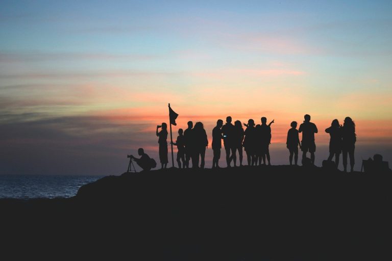 Menschen stehen silhouettenhaft am Strand bei Sonnenuntergang.